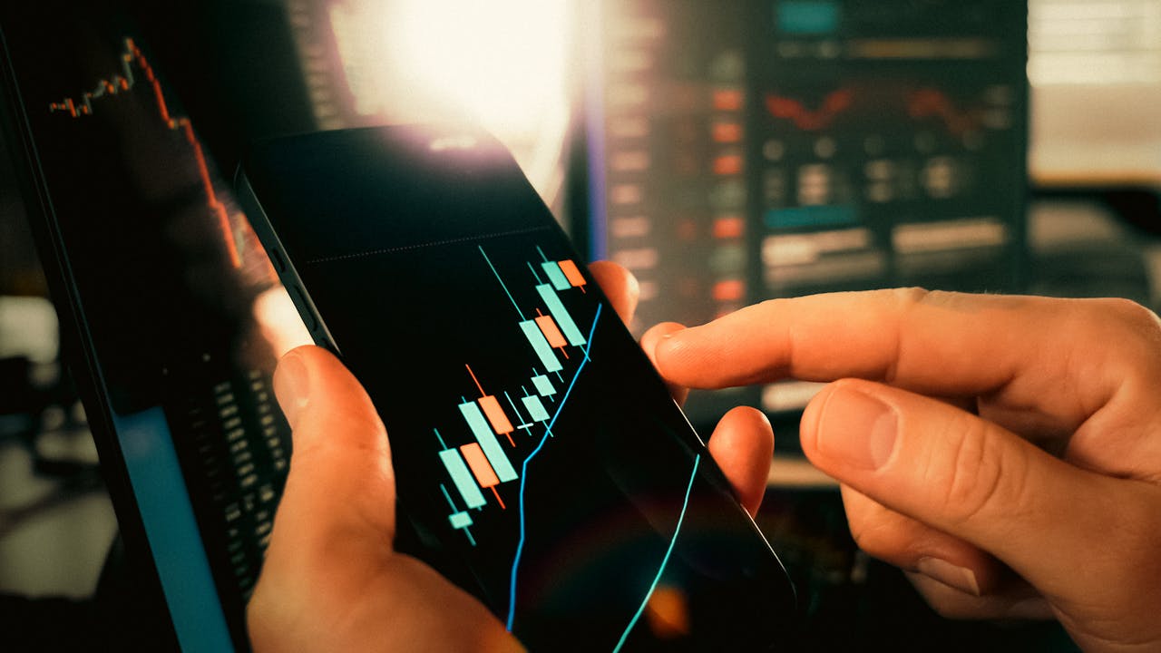 Hands interacting with financial charts on a smartphone, showcasing stock market trends.