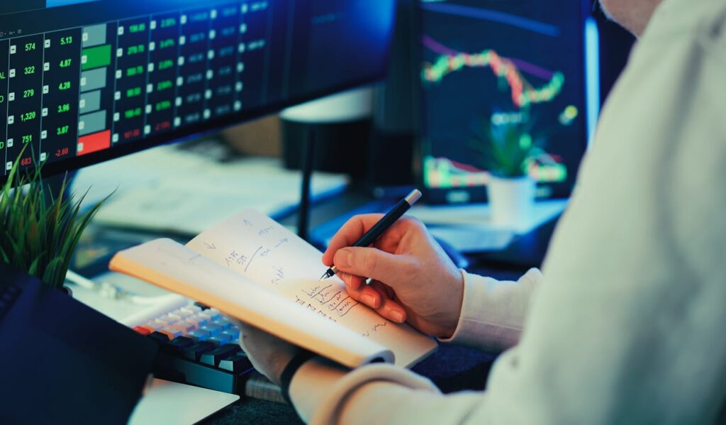 pexels-photo-36496955 Person analyzing financial data on screens, making notes. Ideal for business and finance themes.