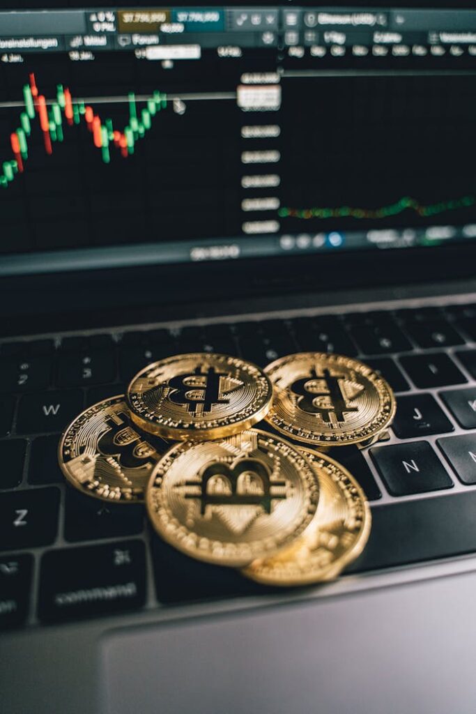 pexels-photo-6770521 Golden bitcoins on a laptop keyboard with a trading chart in the background, symbolizing digital currency and finance.